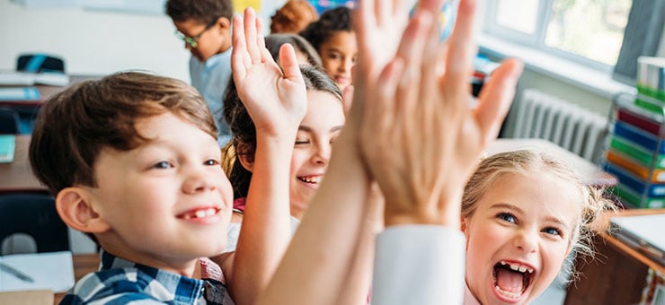 Elementary aged kids giving each other a high five in the classroom.
